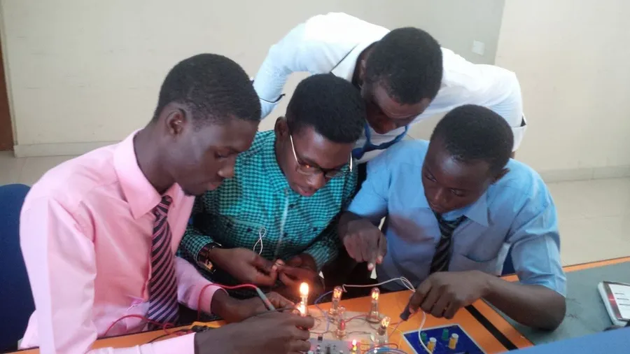 Kenneth and classmates leaning over a lab bench, testing a circuit of small glowing bulbs with probes