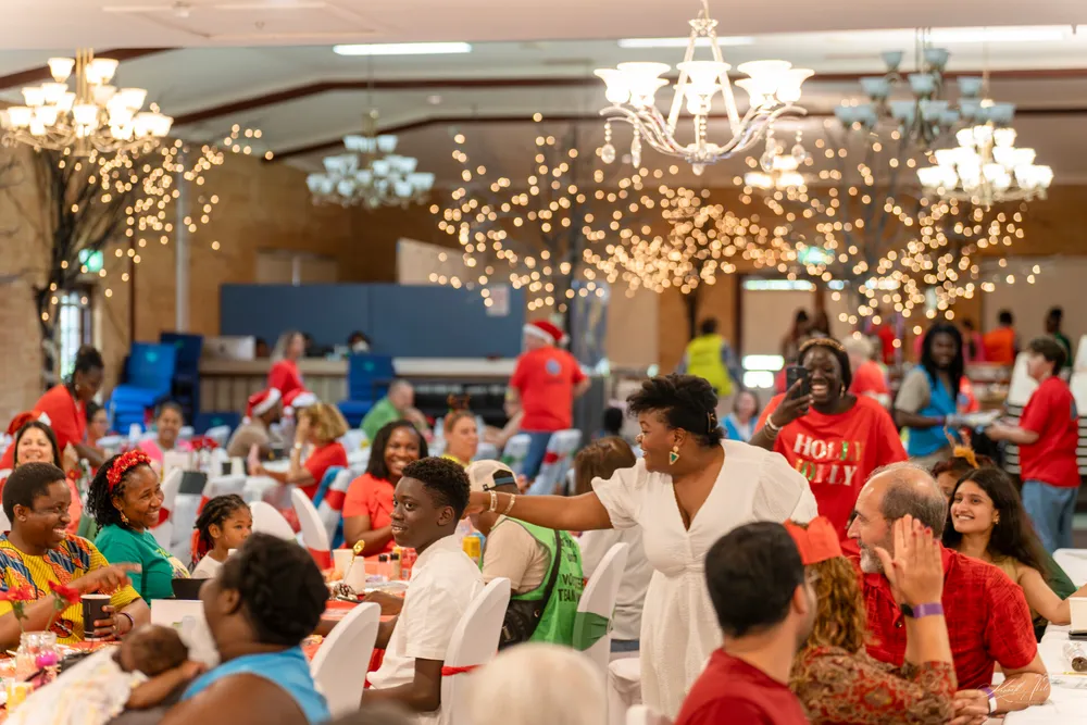 A hall decorated with chandeliers and fairy-light trees, full of guests laughing at long tables while volunteers in red shirts move between them