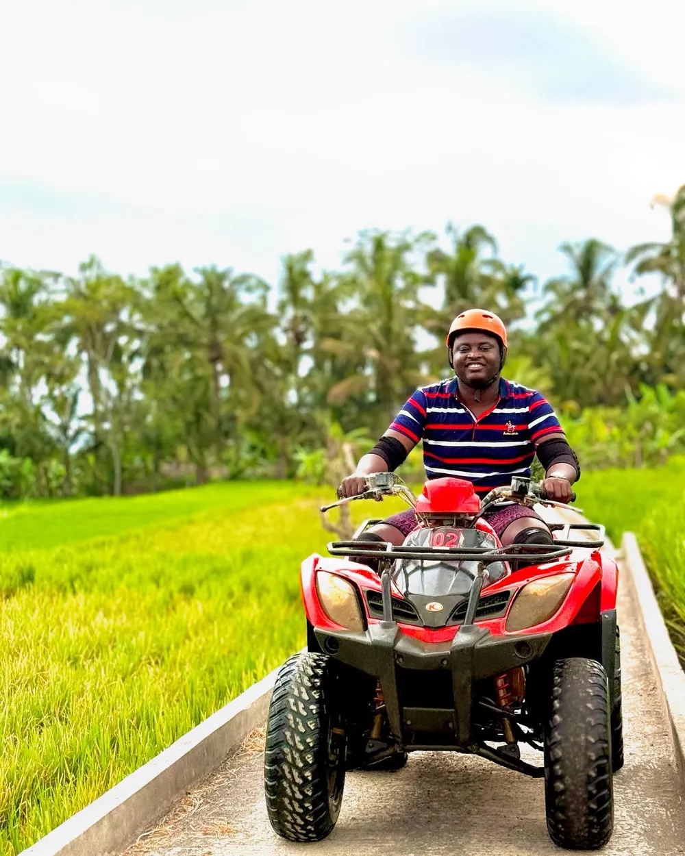 Kenneth riding a red quad bike on a path between palm trees