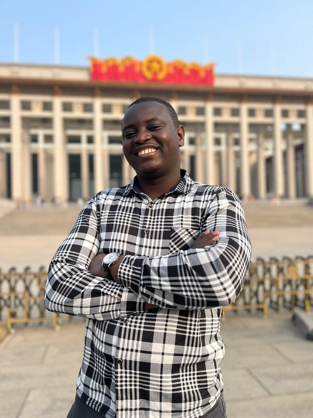 Kenneth in a checked shirt with arms crossed, in front of a grand building with a red banner