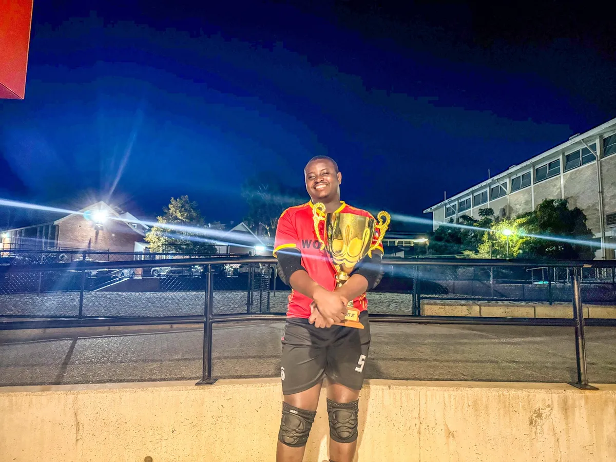 Kenneth in a red Wolves kit and goalkeeper knee pads, holding a gold trophy at a floodlit court at night