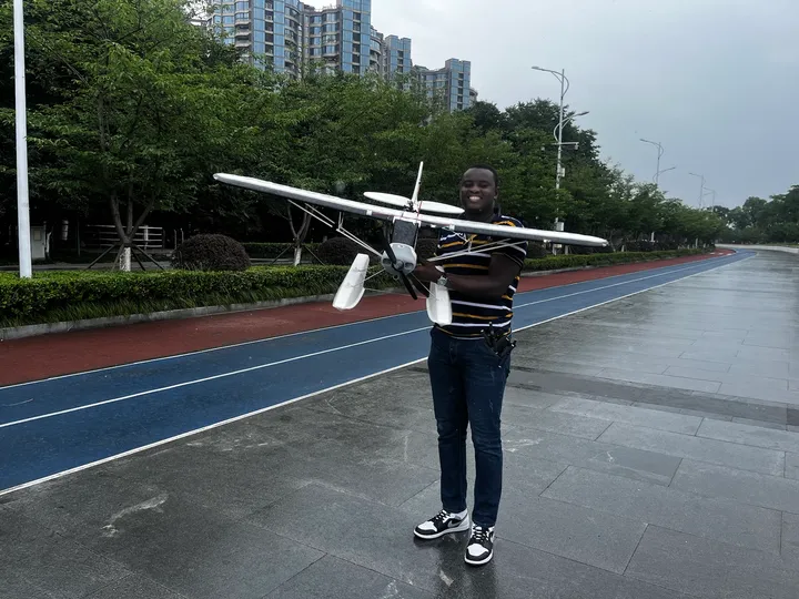 Kenneth standing on a running track holding a white fixed-wing drone