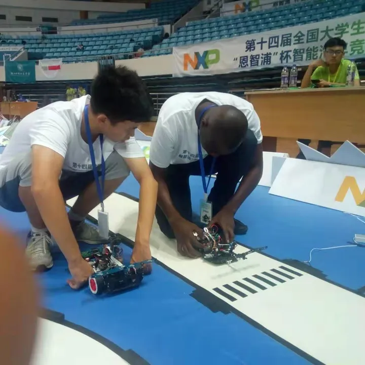 Kenneth and a teammate kneeling on the track, adjusting a small autonomous car at the NXP smart car competition