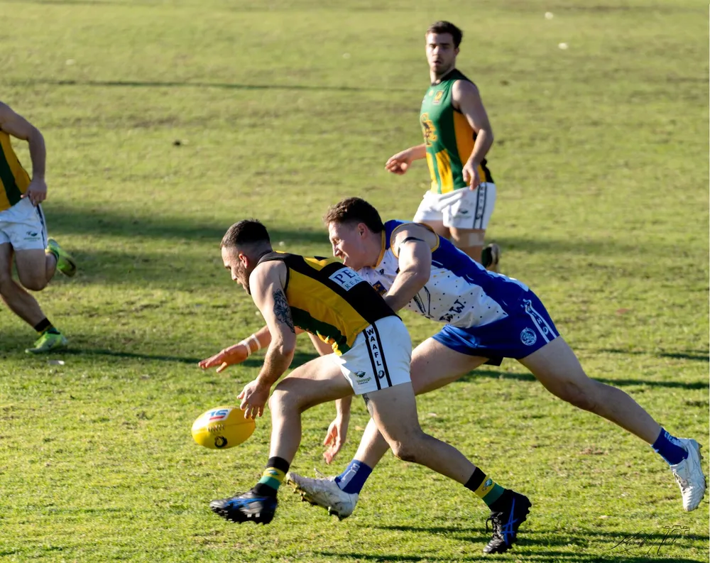 Australian rules players diving for a yellow ball on the grass